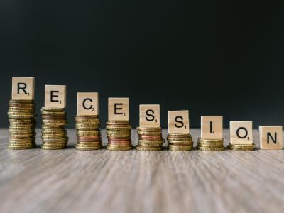 Opgestapelde euromunten met scrabbleletters vormen het woord recessie op een houten tafel.