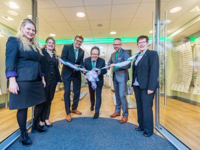 Verschillende mensen in nette kleding knippen ceremonieel een lint door bij de opening van een Specsavers-winkel.