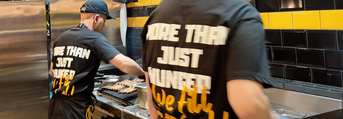 Medewerkers van Kingribs bereiden ribs in een keuken met zwarte en gele wandtegels.