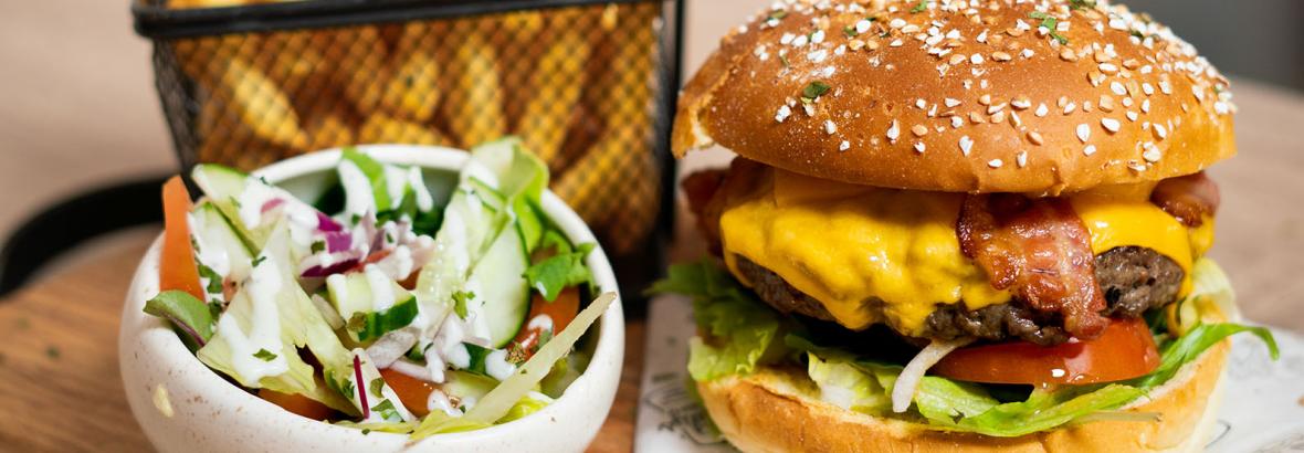 Burger met spek en kaas, geserveerd met een portie friet en frisse salade op een houten plank.