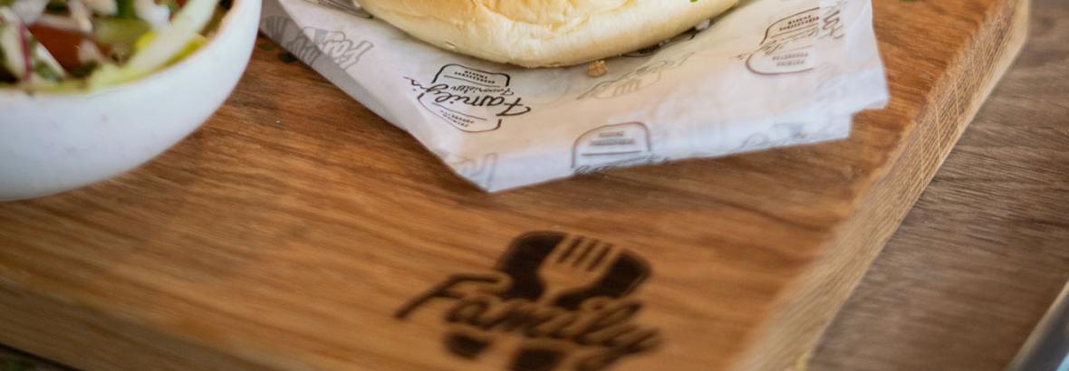 Hamburger met kaas en bacon, geserveerd op houten plank met frieten en salade op de voorgrond in familiecafetaria.