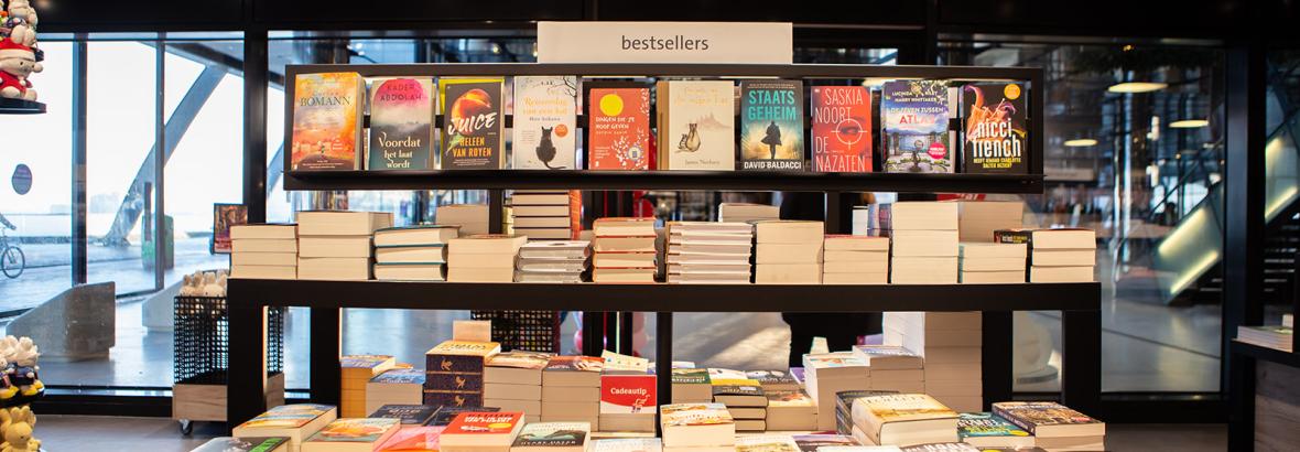 Bestsellers boekenpresentatie in een Bruna-winkel met meerdere stapels en rijen boeken op planken.