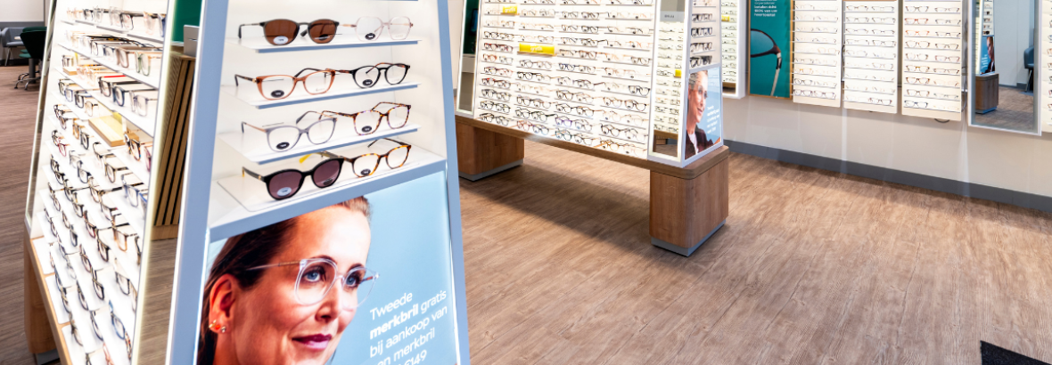Winkelvloer van Specsavers met displays vol brillen en promotieposter met vrouw die een bril draagt.