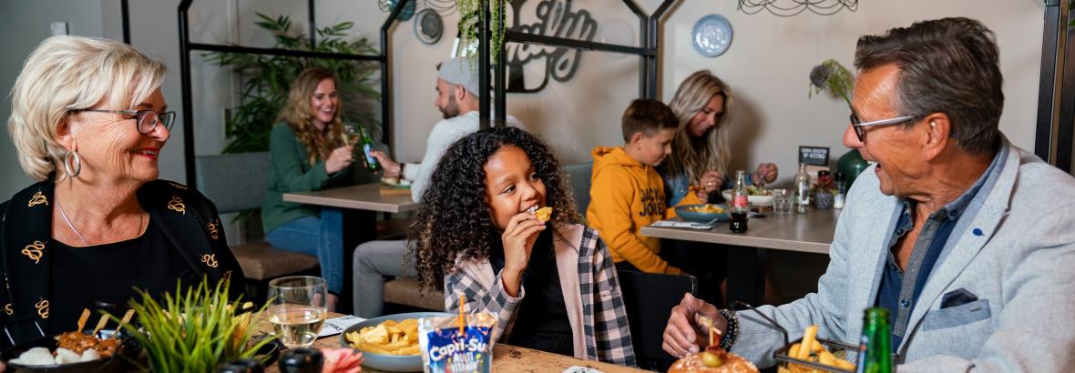 Gezellige families genieten van maaltijden in een moderne cafetaria met hamburgers, frietjes en drankjes.